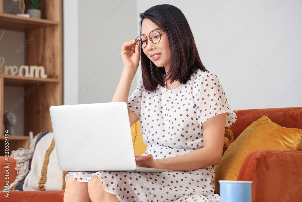 Beautiful Asian woman in stylish eyeglasses using laptop at home