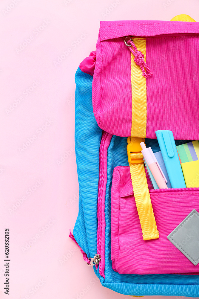 Color school backpack with notebooks and stationery on pink background