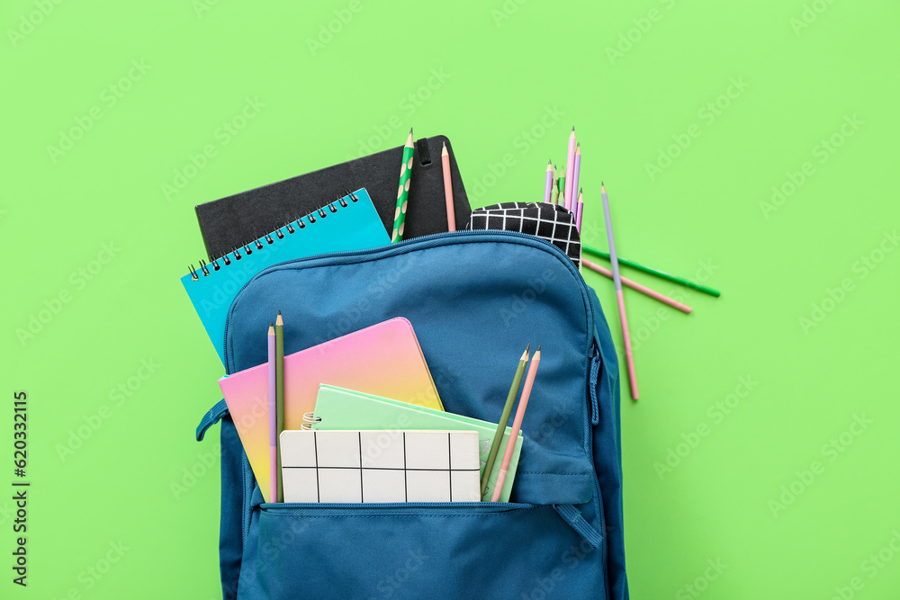 Blue school backpack with notebooks and pencils on green background