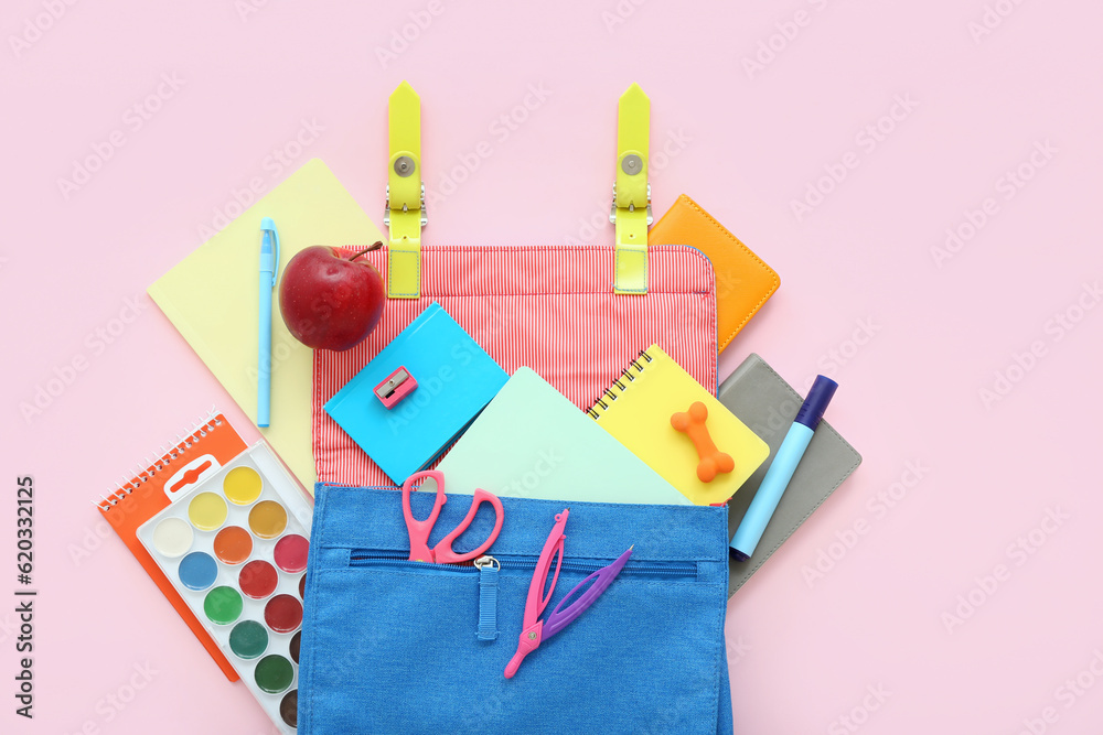 Blue school backpack with notebooks, watercolors and apple on pink background