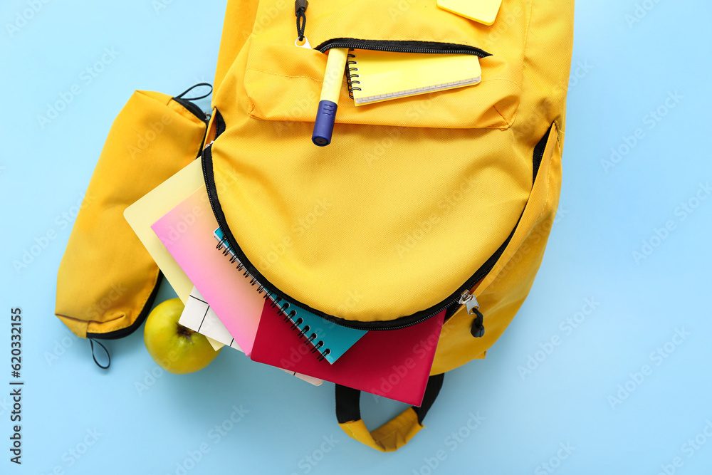 Yellow school backpack with pencil case, notebooks and apple on blue background