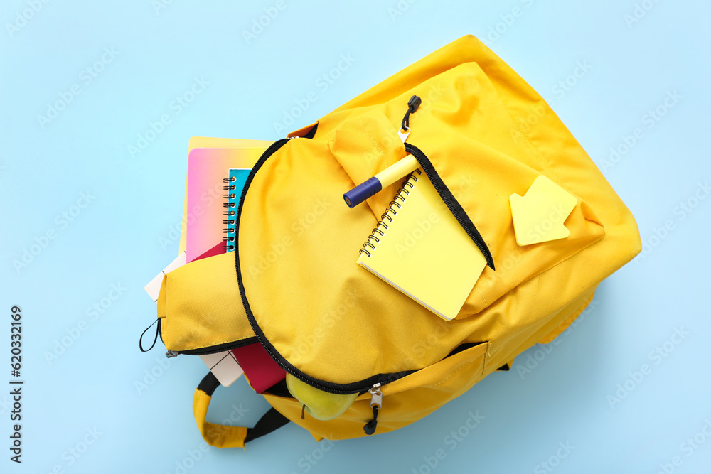 Yellow school backpack with pencil case, notebooks and apple on blue background