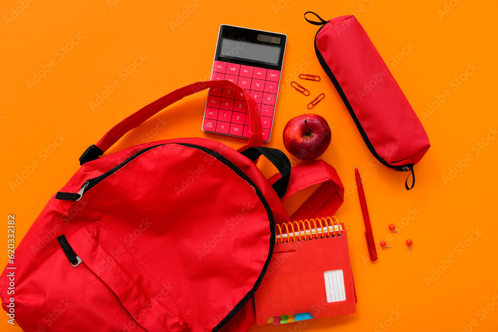 Red school backpack with pencil case, calculator and apple on orange background