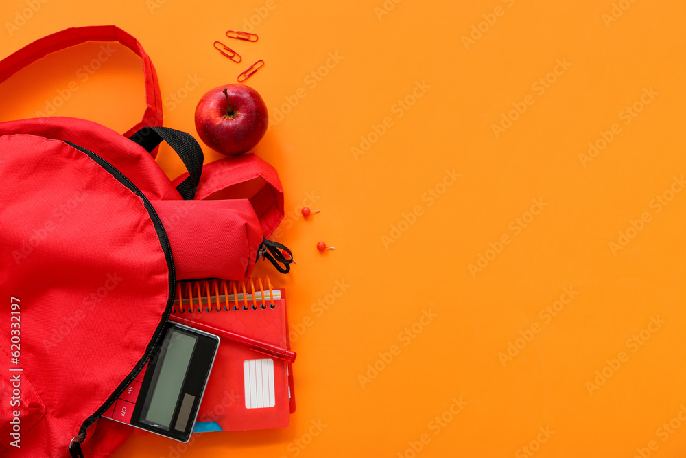 Red school backpack with pencil case, calculator and apple on orange background