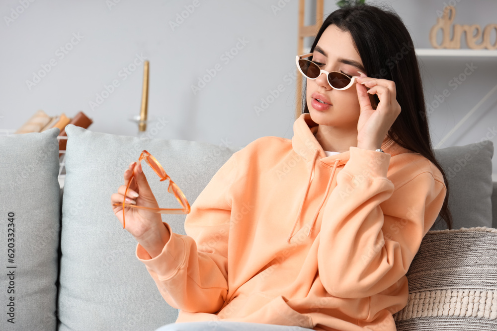 Young woman trying on different stylish sunglasses at home