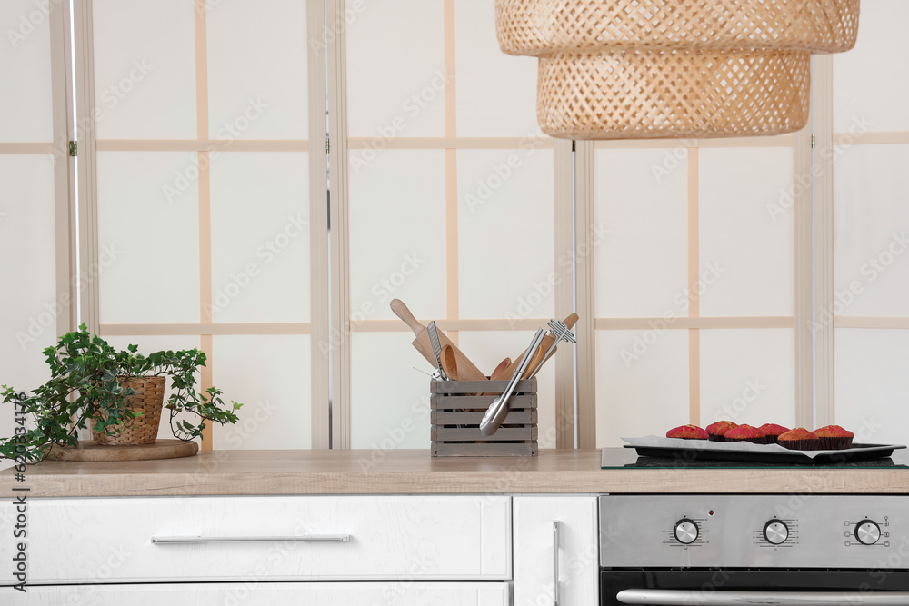 Tray with fresh muffins, utensils and houseplant on wooden kitchen counter