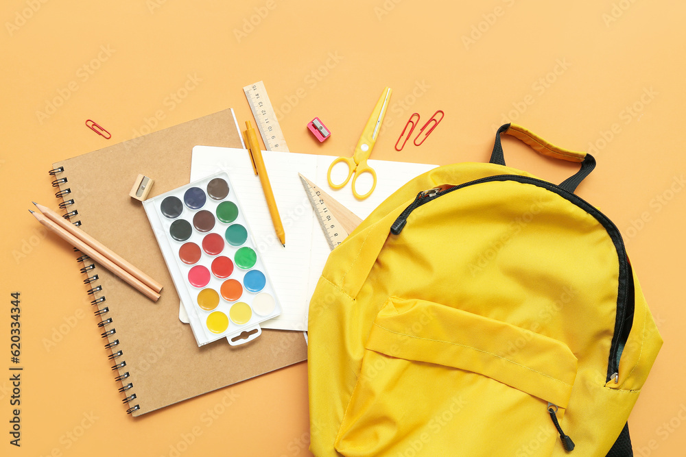 School backpack with paints and stationery on orange background