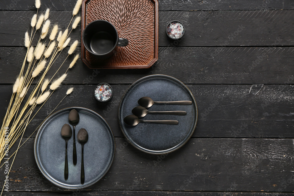 Clean plates with set of spoons and dried lagurus on black wooden table