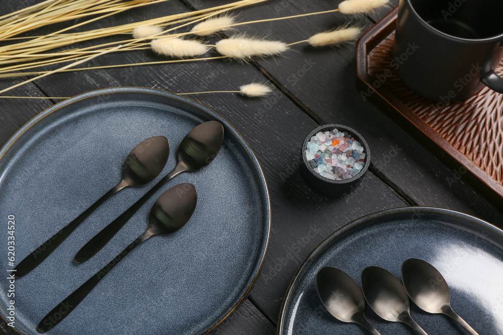 Clean plates with set of spoons and dried lagurus on black wooden table