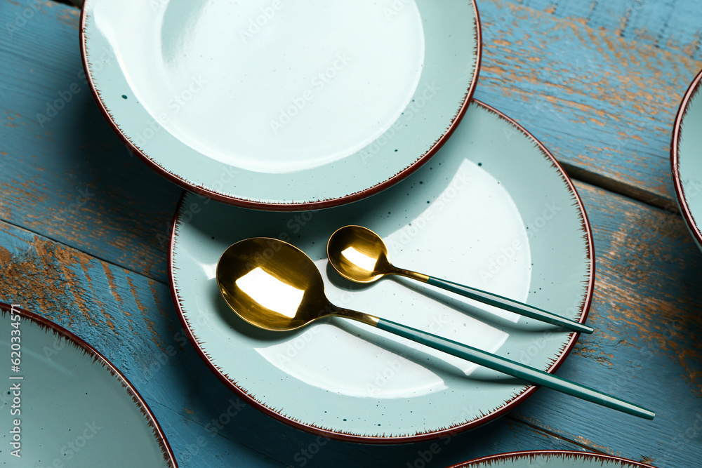 Clean plates and golden spoons on blue wooden table