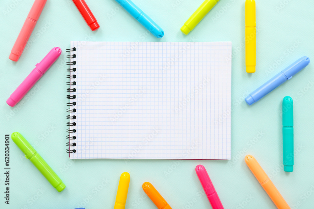 Blank notebook with different colorful markers on blue background