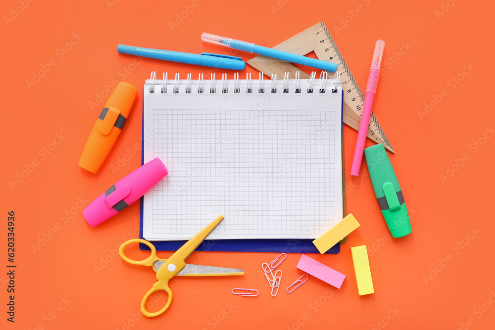 Blank notebook with different stationery on orange background