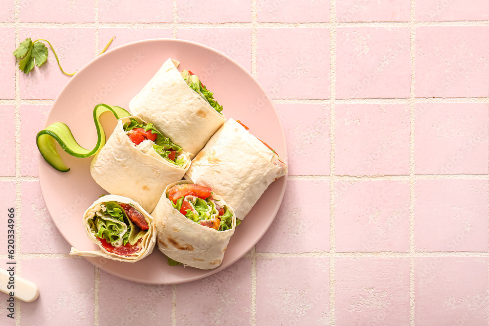 Plate of tasty lavash rolls with tomatoes and greens on pink tile background