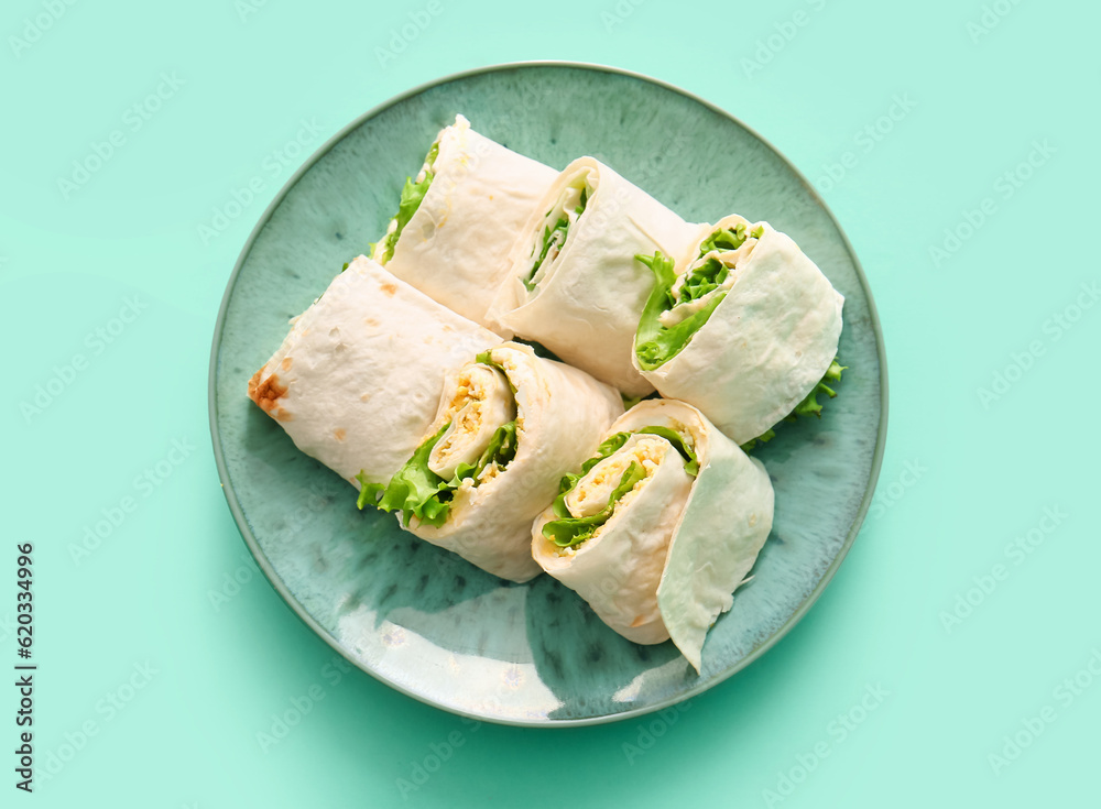 Plate of tasty lavash rolls with egg and greens on turquoise background