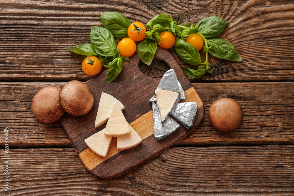 Board with triangles of tasty processed cheese and vegetables on wooden background