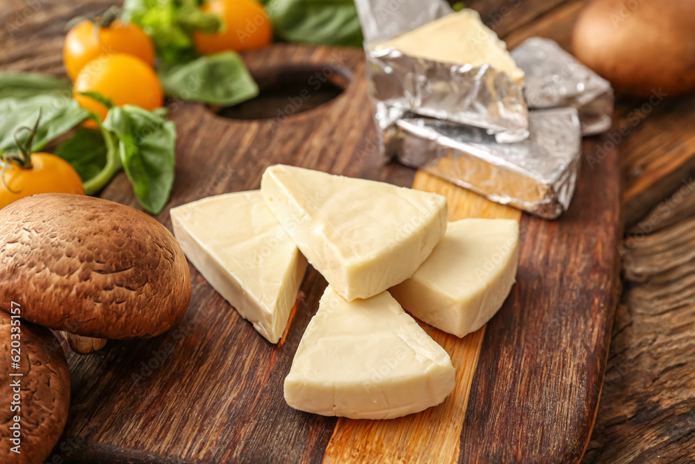 Board with triangles of tasty processed cheese and vegetables on table, closeup