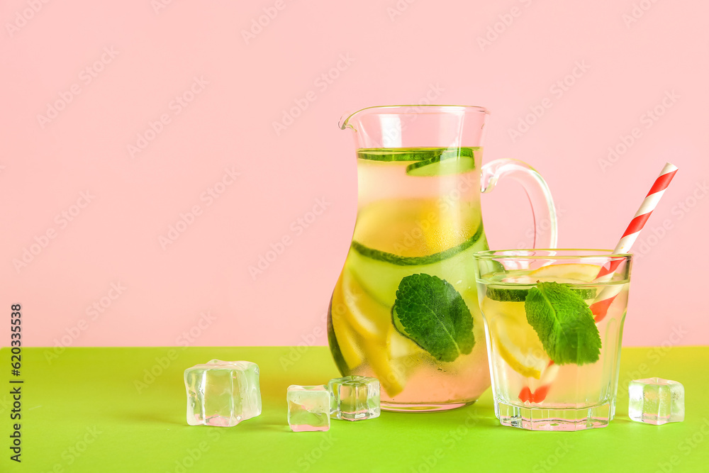 Jug and glass of lemonade with cucumber on green table