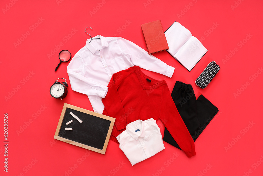 Composition with stylish school uniform, chalkboard, alarm clock and stationery on red background