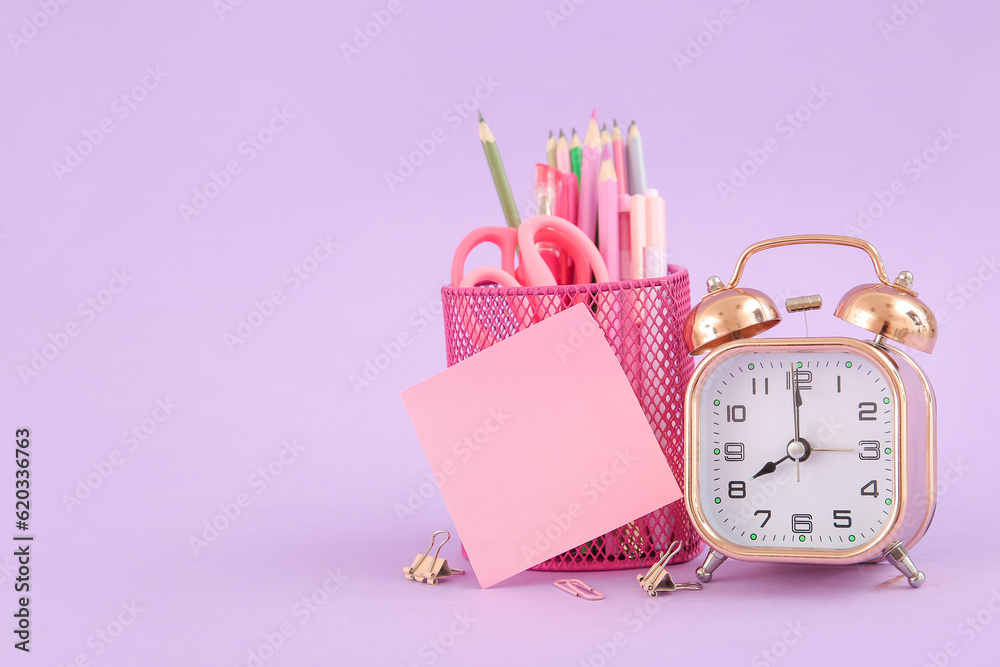 Alarm clock with different stationery on lilac background