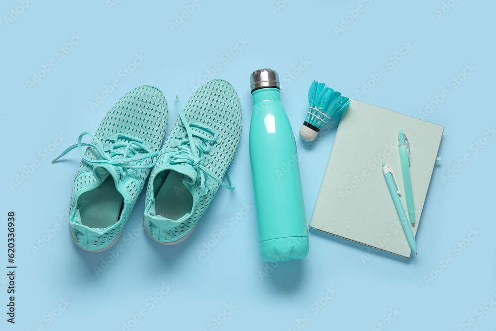 Sneakers with bottle of water, badminton shuttlecock and stationery on blue background