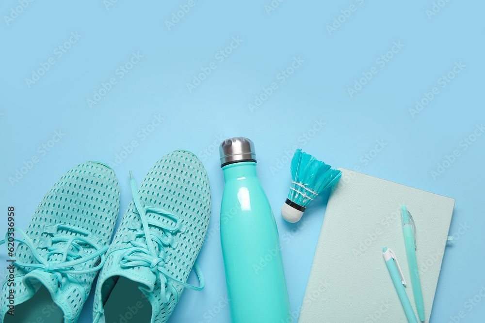 Sneakers with bottle of water, badminton shuttlecock and stationery on blue background