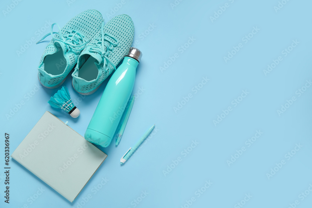 Sneakers with bottle of water, badminton shuttlecock and stationery on blue background