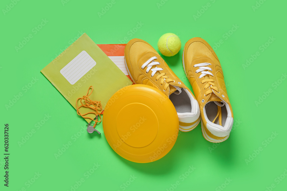 Sneakers with frisbee, tennis ball, whistle and notebooks on green background