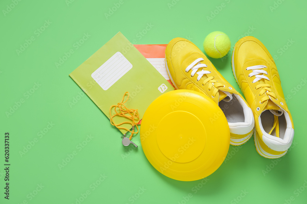 Sneakers with frisbee, tennis ball, whistle and notebooks on green background