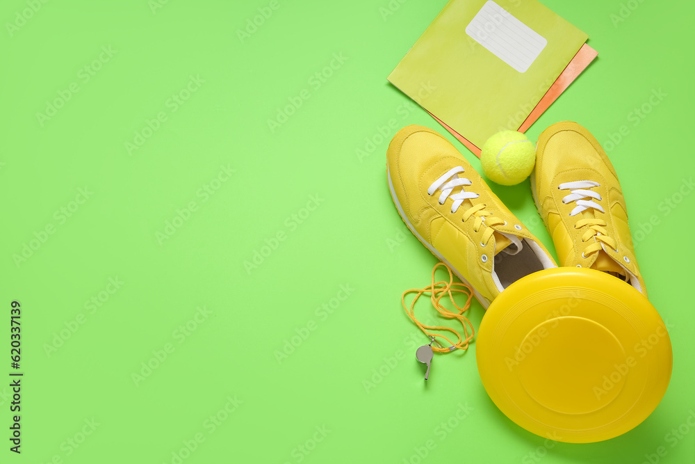 Sneakers with frisbee, tennis ball, whistle and notebooks on green background