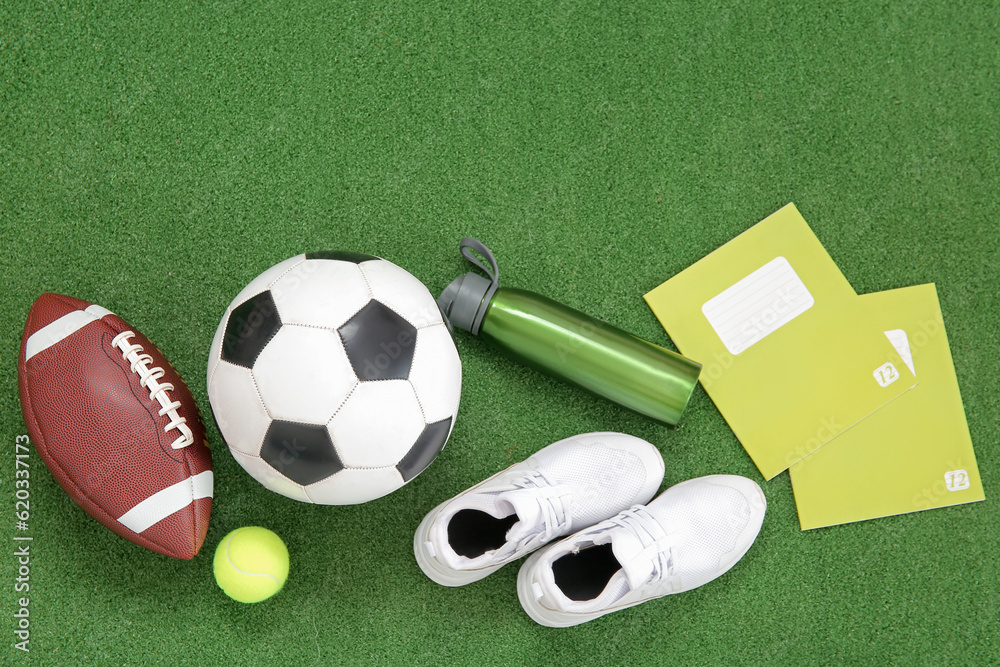 Sneakers with sport balls, bottle of water and notebooks on color background