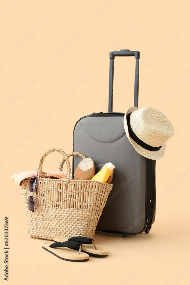 Suitcase with wicker hat, bag and beach accessories on pale orange background. Travel concept