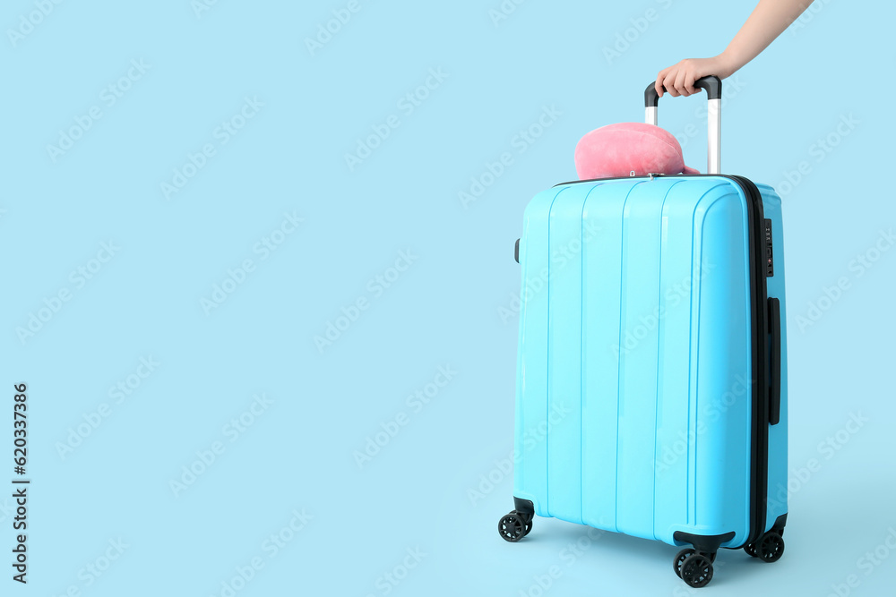 Female hand with suitcase and travel cushion on blue background. Travel concept