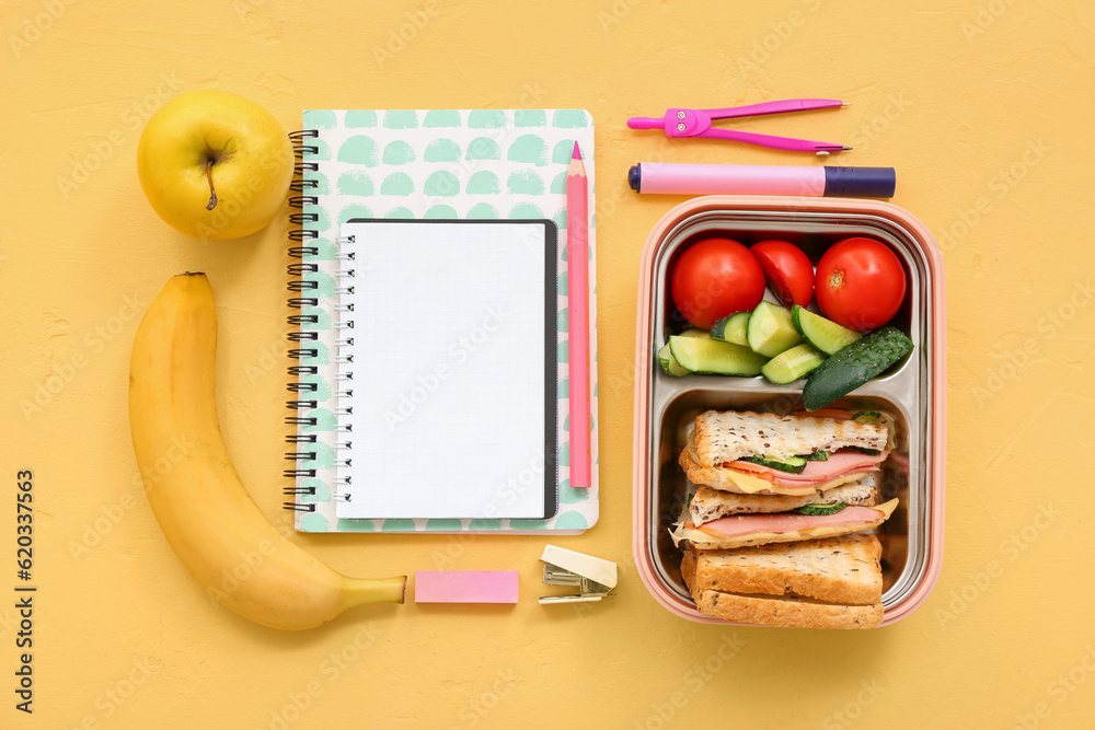 Different stationery and lunch box with tasty food on yellow background