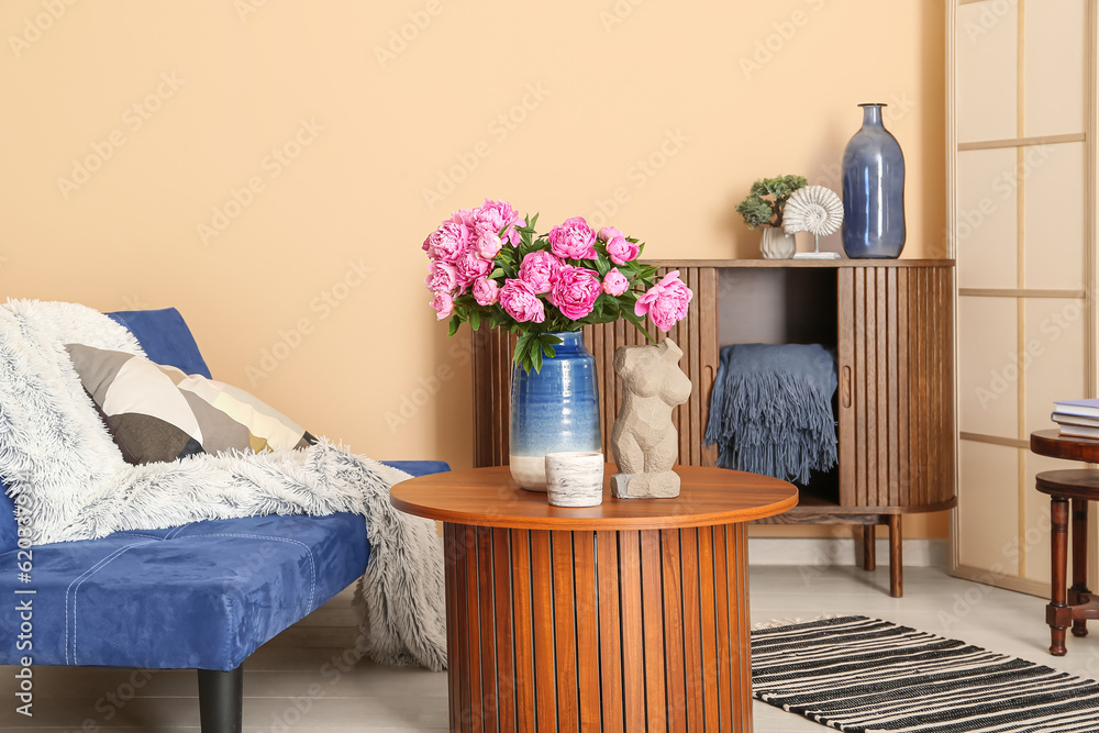 Vase of pink peonies on coffee table, couch and dresser near beige wall