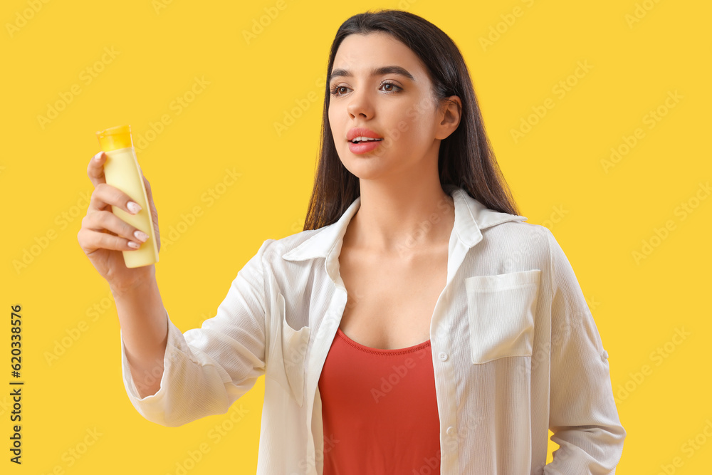 Young woman with sunscreen cream on yellow background