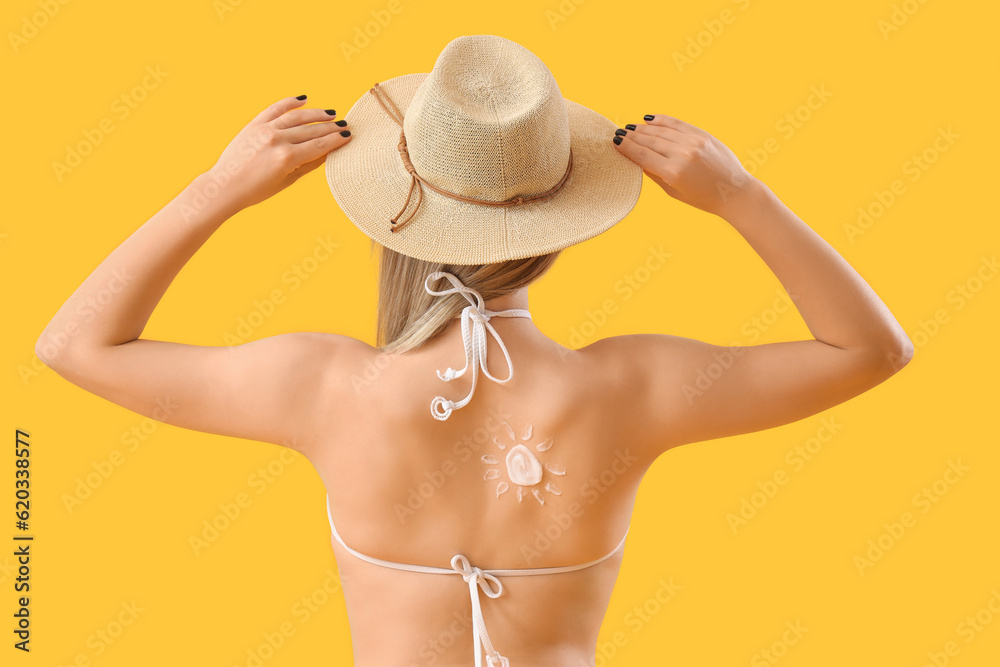 Young woman with sun made of sunscreen cream on her back against yellow background