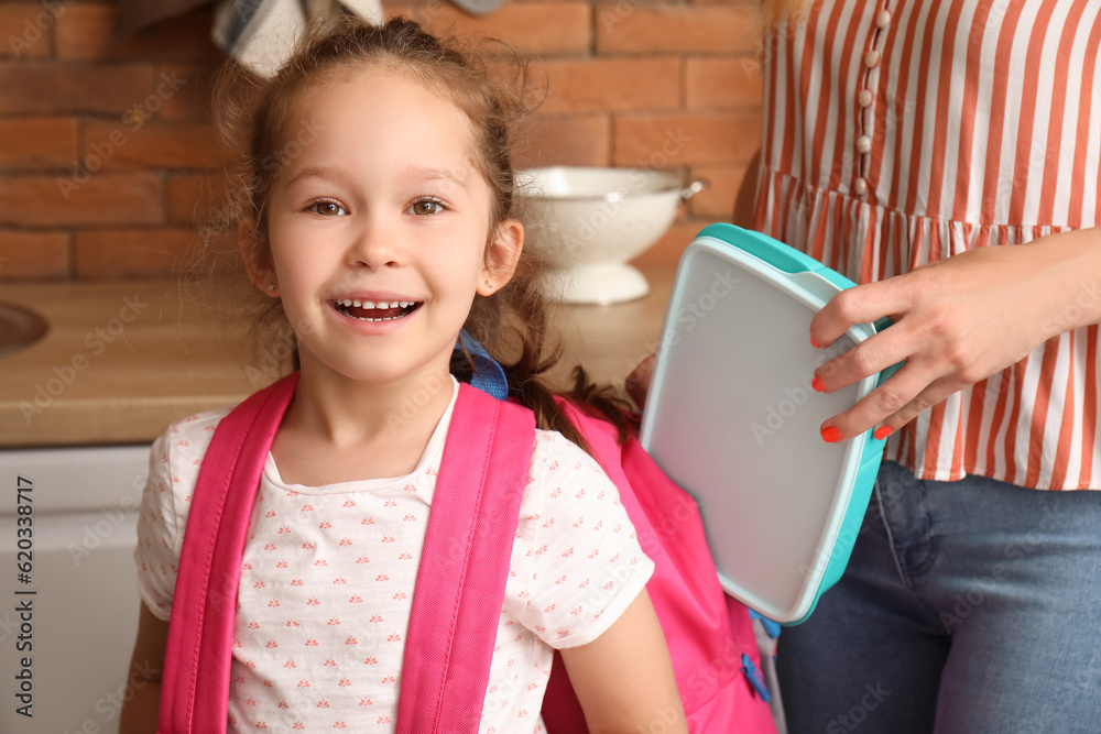 Mother packing school lunch for her little daughter in kitchen, closeup