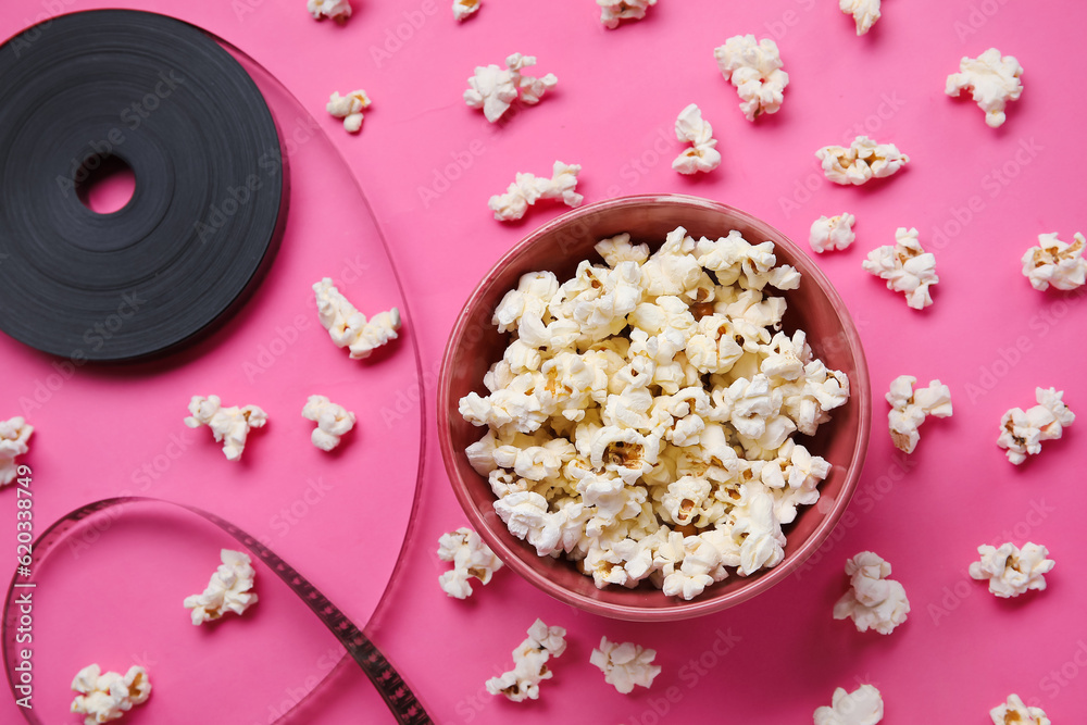 Bowl with tasty popcorn and film reel on pink background