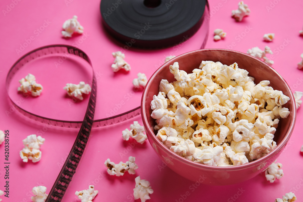 Bowl with tasty popcorn and film reel on pink background