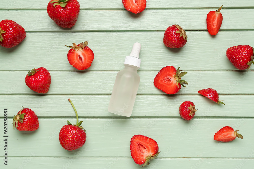 Bottle with cosmetic oil and strawberries on green wooden background