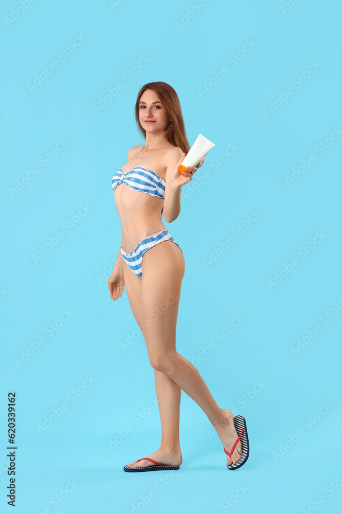 Young woman with sunscreen cream on blue background