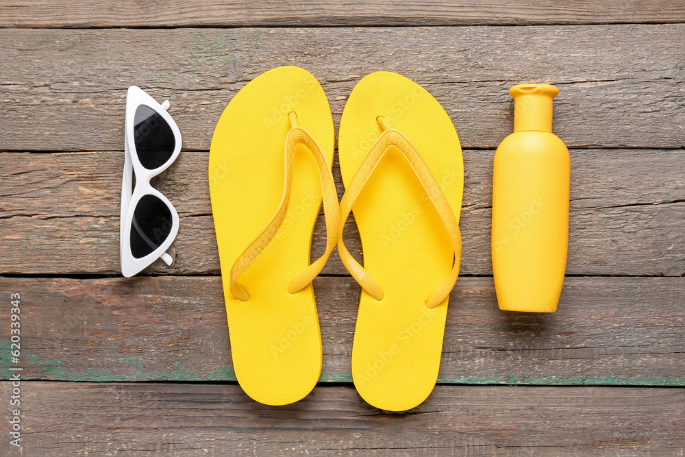 Sunglasses with flip flops and bottle of sunscreen cream on brown wooden background