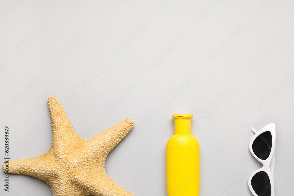 Sunglasses with starfish and bottle of sunscreen cream on grey background