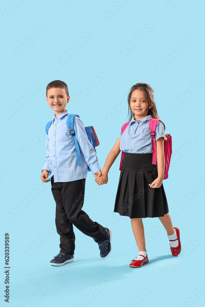 Little schoolchildren holding hands on light blue background