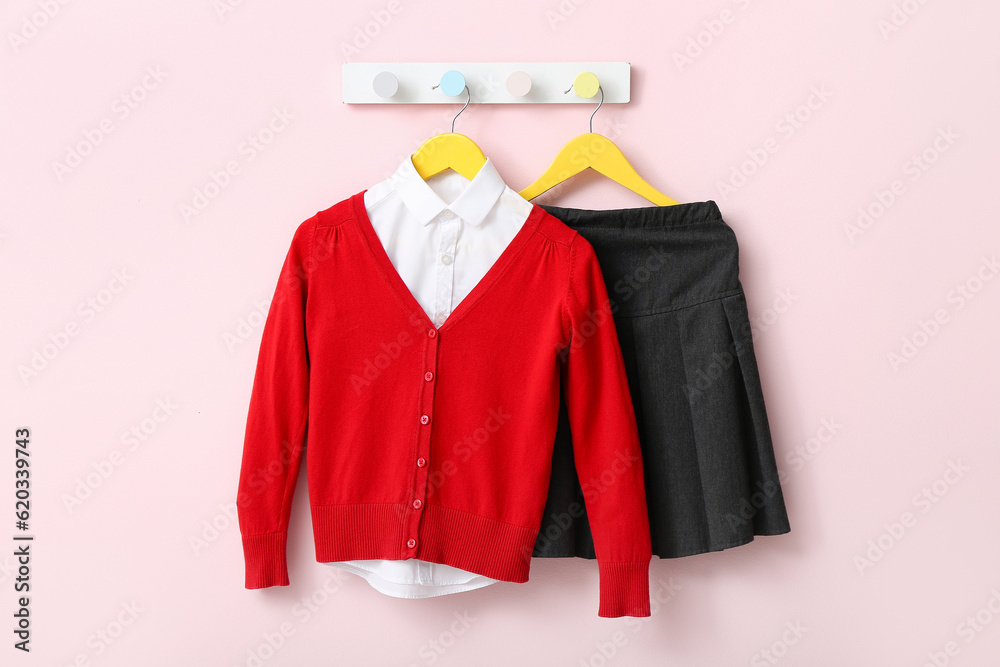 Stylish school uniform hanging on rack against pink wall