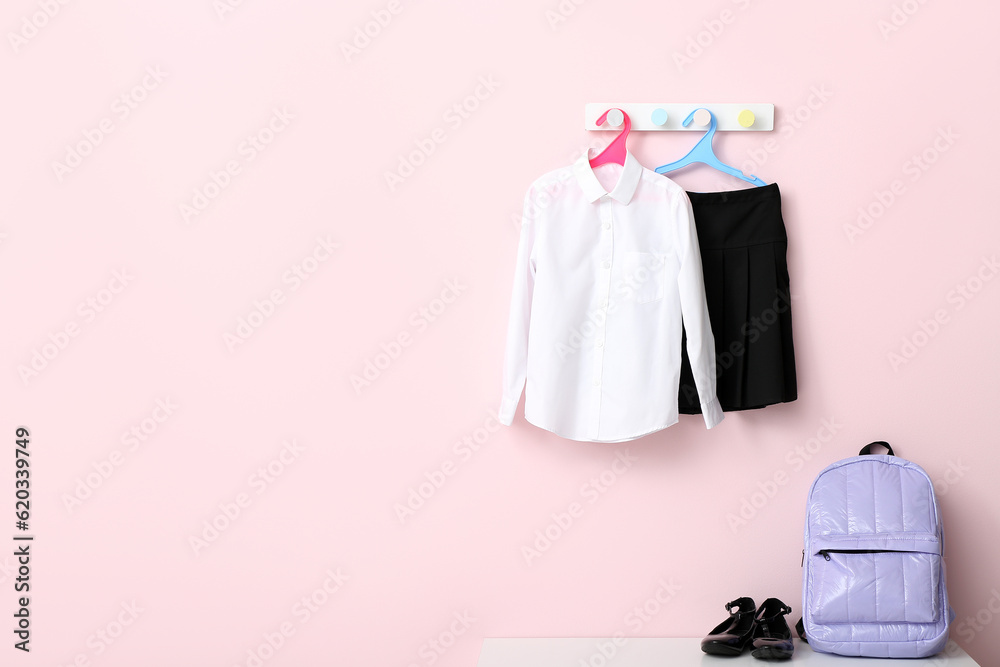 Stylish school uniform hanging on rack with backpack against pink wall