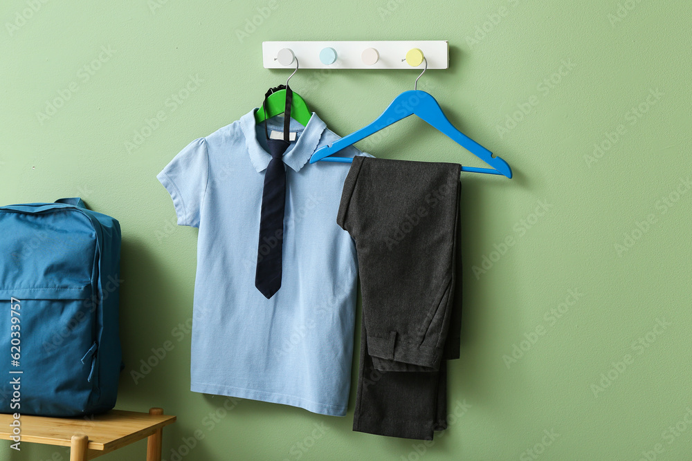 Stylish school uniform hanging on rack with backpack against green wall