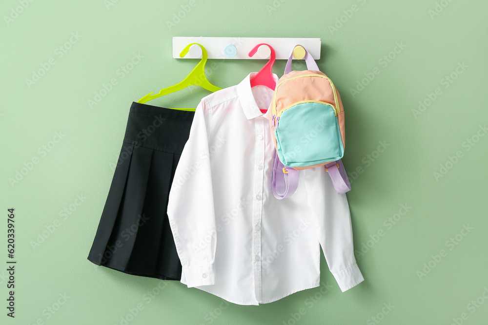 Stylish school uniform with backpack hanging on rack against green wall