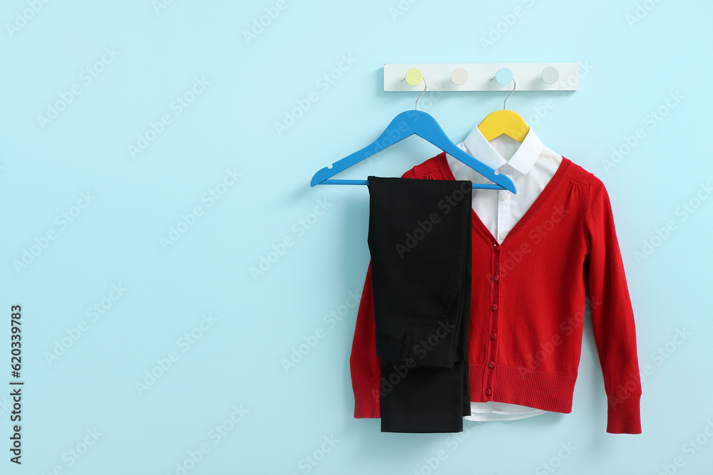 Stylish school uniform hanging on rack against blue wall