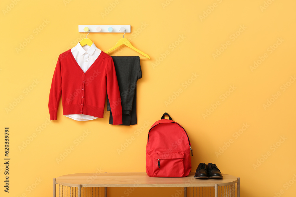 Stylish school uniform hanging on rack with backpack against yellow wall